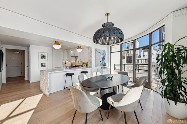 dining space with light wood-type flooring, an inviting chandelier, and sink