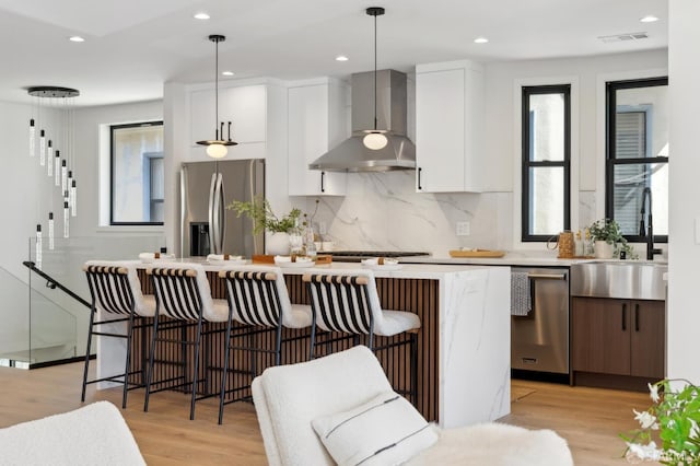 867 33rd Ave, San Francisco, CA 94121 - kitchen with wall chimney range hood, appliances with stainless steel finishes, a sink, white cabinetry, and a breakfast bar area