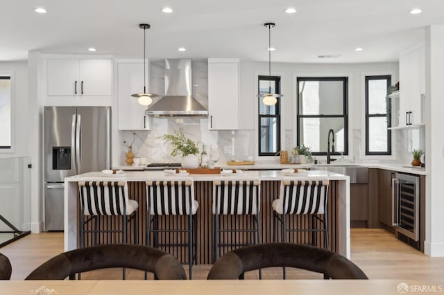 867 33rd Ave, San Francisco, CA 94121 - kitchen with stainless steel refrigerator with ice dispenser, wall chimney range hood, beverage cooler, light countertops, and light wood-type flooring