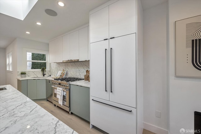 kitchen with tasteful backsplash, sink, light hardwood / wood-style flooring, a skylight, and stainless steel gas range