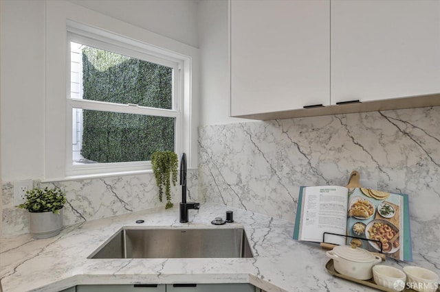 interior details featuring light stone countertops, sink, white cabinetry, and decorative backsplash