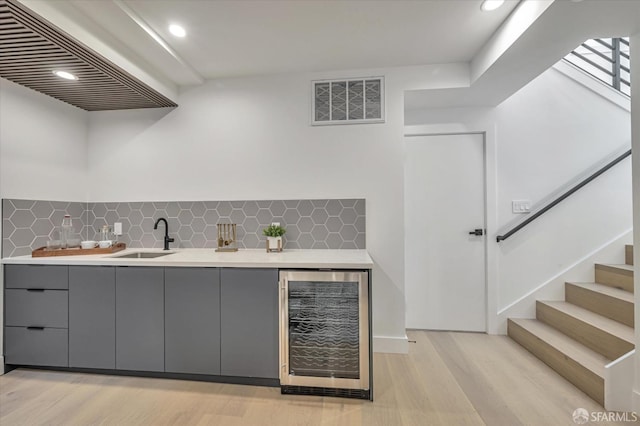 bar with beverage cooler, tasteful backsplash, light hardwood / wood-style floors, sink, and gray cabinets