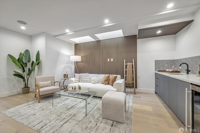 living room featuring a skylight, light hardwood / wood-style floors, beverage cooler, and sink