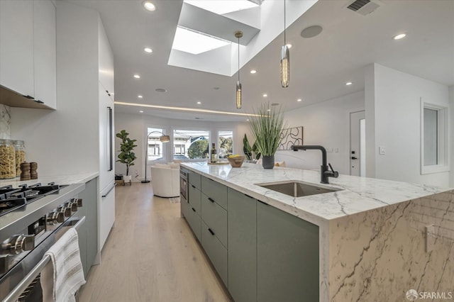 kitchen with white cabinetry, a center island with sink, pendant lighting, high end stainless steel range, and sink