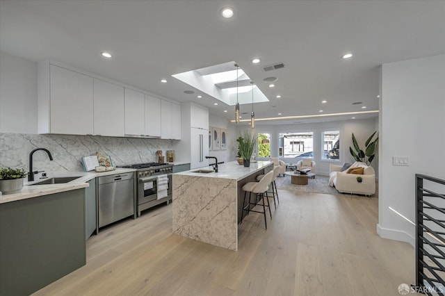 kitchen featuring a breakfast bar, sink, an island with sink, stainless steel appliances, and white cabinets