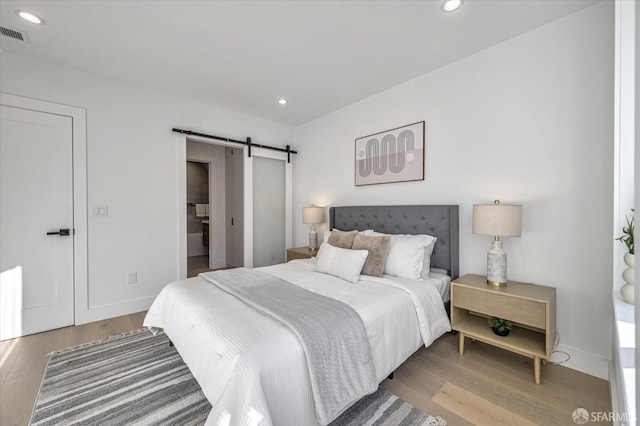 bedroom with a barn door and light wood-type flooring