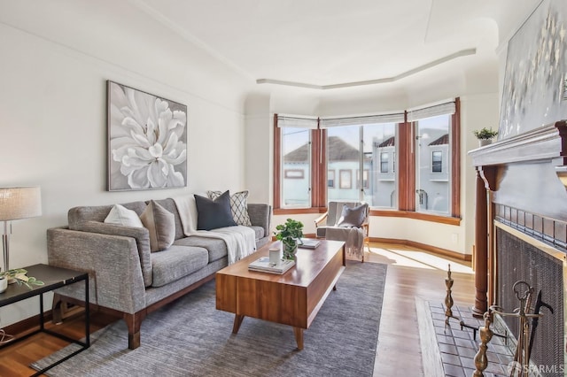 living room with a fireplace with raised hearth, baseboards, and wood finished floors