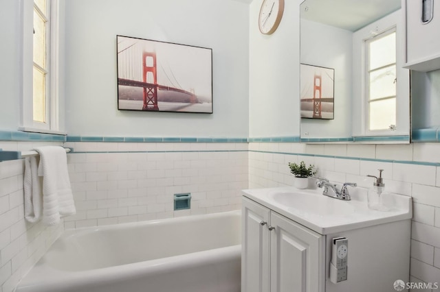 full bath with vanity, wainscoting, a bathing tub, and tile walls