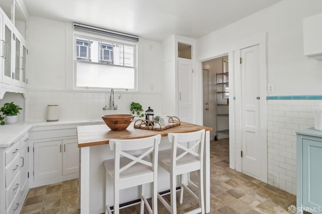 kitchen with a sink, glass insert cabinets, wooden counters, and tile walls
