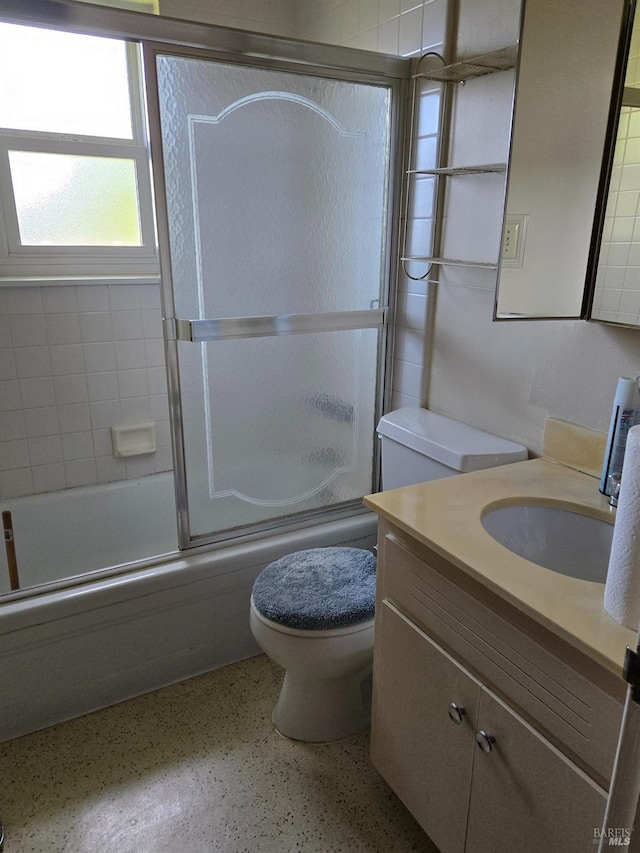bathroom with shower / bath combination with glass door, speckled floor, toilet, and vanity