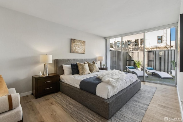 bedroom with floor to ceiling windows, access to outside, and light hardwood / wood-style floors