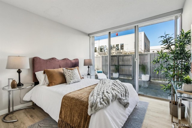 bedroom featuring expansive windows, light hardwood / wood-style floors, and access to outside