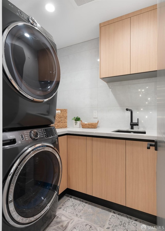 laundry area with cabinets, stacked washer and dryer, and sink