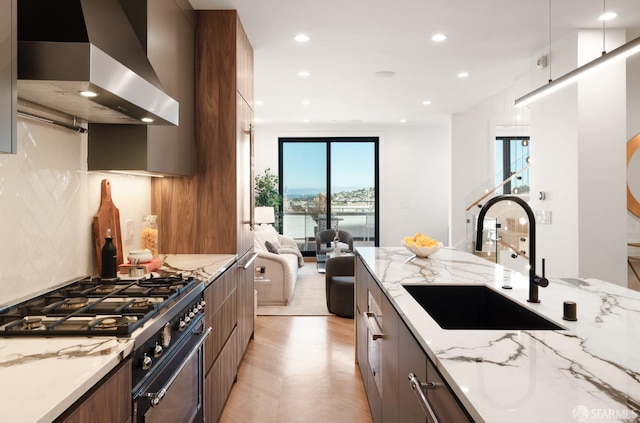 kitchen featuring sink, light stone counters, stainless steel range, light parquet flooring, and range hood