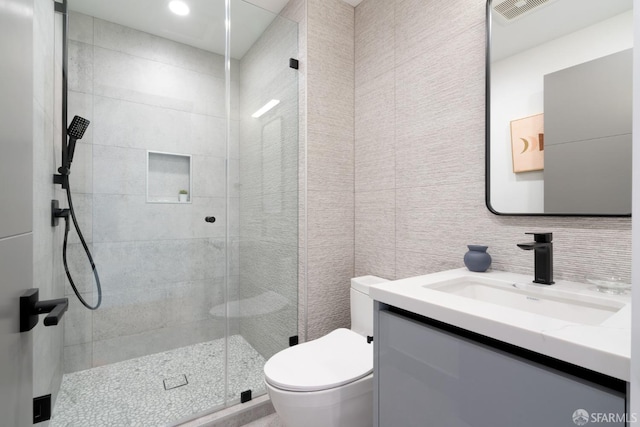 bathroom with toilet, a shower with shower door, tasteful backsplash, tile walls, and vanity