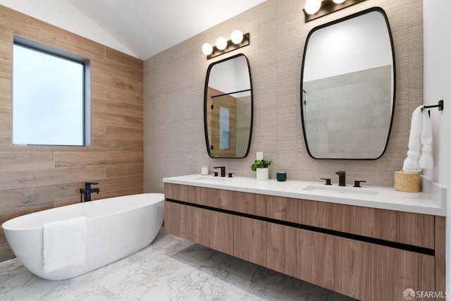 bathroom with vanity, a bathing tub, vaulted ceiling, and tile walls