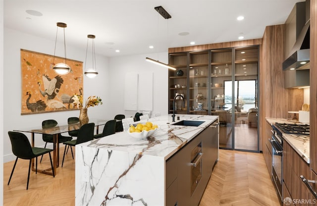 kitchen with a large island with sink, hanging light fixtures, sink, and light parquet floors