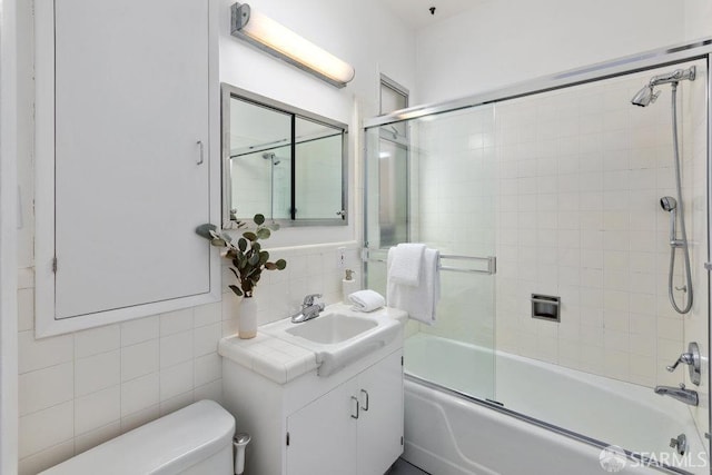 bathroom featuring tile walls, bath / shower combo with glass door, backsplash, toilet, and vanity