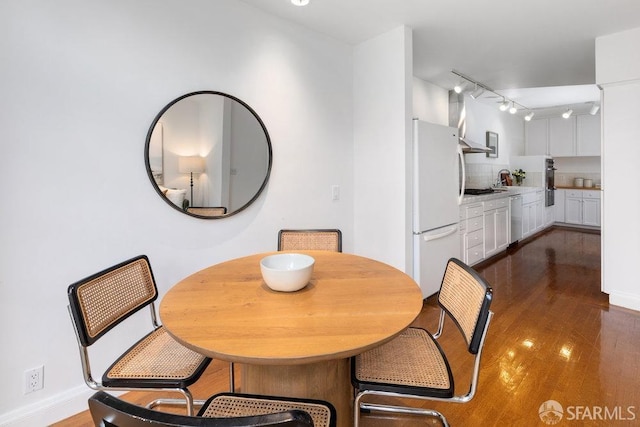 dining space featuring rail lighting, baseboards, and dark wood-style flooring