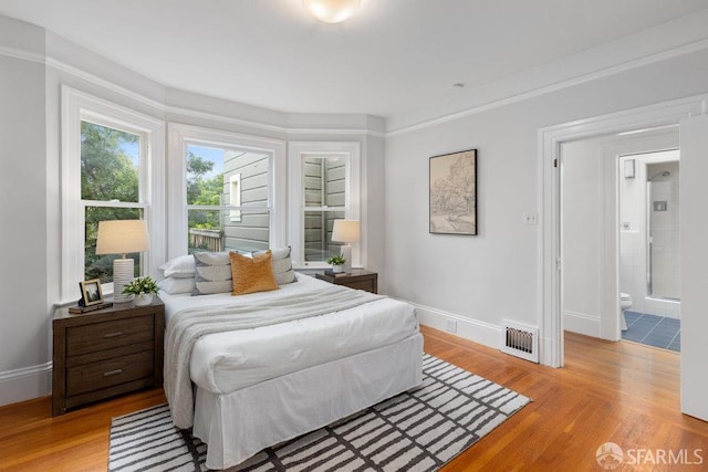 bedroom with visible vents, light wood-style flooring, baseboards, and ensuite bathroom