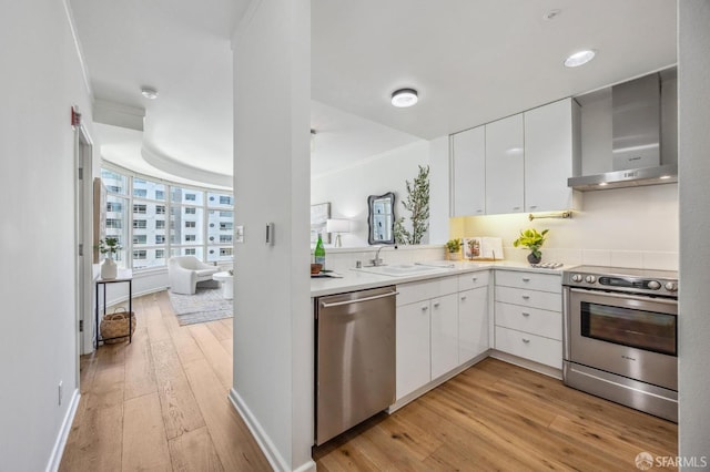 kitchen with light hardwood / wood-style floors, appliances with stainless steel finishes, wall chimney range hood, white cabinets, and sink