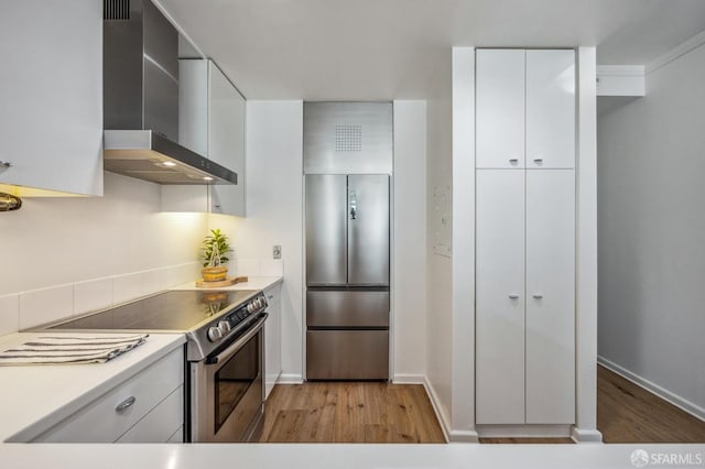 kitchen with white cabinets, wall chimney range hood, stainless steel appliances, and light hardwood / wood-style floors