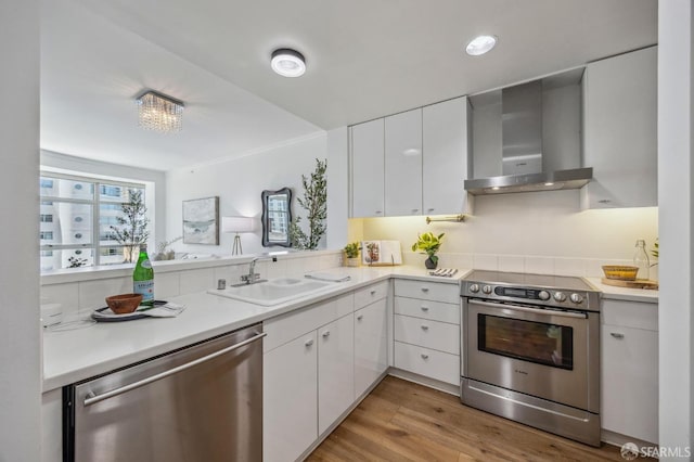 kitchen featuring white cabinetry, appliances with stainless steel finishes, wall chimney range hood, light hardwood / wood-style flooring, and sink