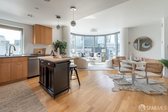 kitchen with light hardwood / wood-style floors, sink, decorative light fixtures, stainless steel dishwasher, and a center island