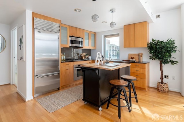 kitchen featuring pendant lighting, light wood-type flooring, appliances with stainless steel finishes, and a kitchen island with sink