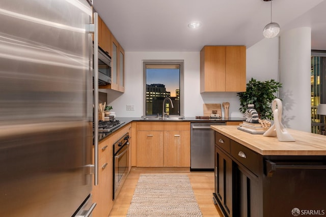 kitchen with light hardwood / wood-style flooring, sink, wood counters, appliances with stainless steel finishes, and decorative light fixtures