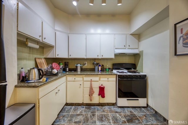 kitchen featuring backsplash, dark stone counters, gas range gas stove, and white cabinets