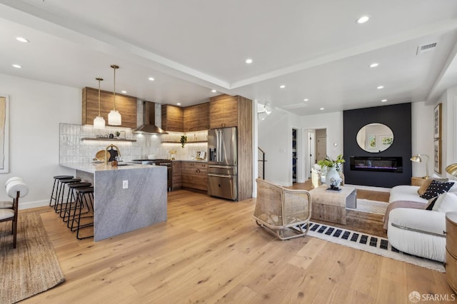 57 Niagara Ave, San Francisco, CA 94112 - kitchen with appliances with stainless steel finishes, wall chimney range hood, brown cabinetry, a breakfast bar, and a peninsula