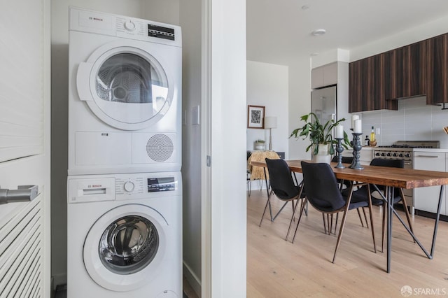 laundry room with stacked washing maching and dryer and light hardwood / wood-style floors