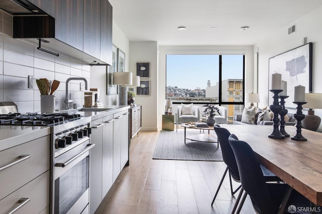 kitchen featuring dark brown cabinetry, sink, tasteful backsplash, light hardwood / wood-style flooring, and stainless steel range with gas cooktop