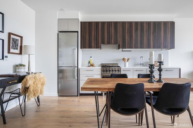 kitchen featuring white cabinetry, dark brown cabinets, appliances with stainless steel finishes, light hardwood / wood-style floors, and decorative backsplash