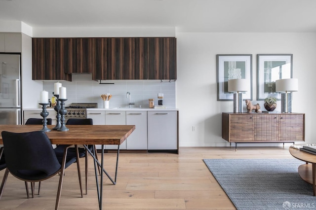 kitchen featuring sink, stainless steel fridge, decorative backsplash, dark brown cabinets, and light wood-type flooring