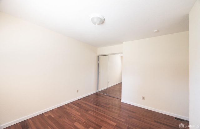 empty room with dark wood finished floors, visible vents, and baseboards