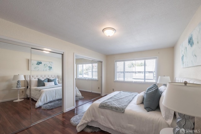 bedroom featuring baseboards, wood finished floors, multiple closets, and a textured ceiling