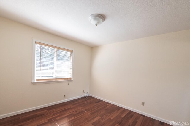 empty room with baseboards, dark wood-type flooring, and a textured ceiling