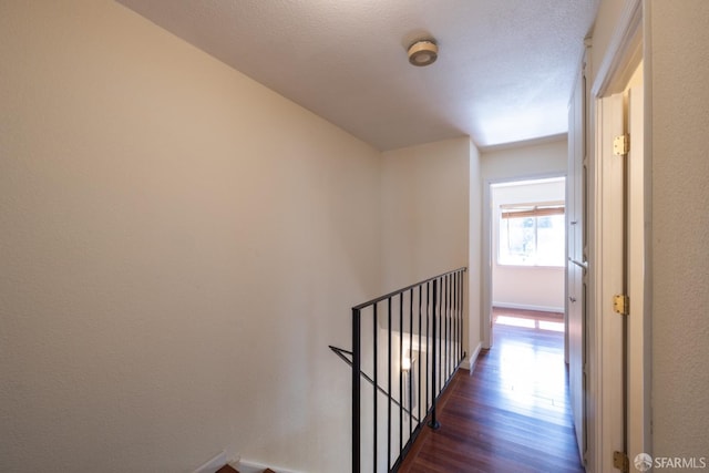 corridor with baseboards, an upstairs landing, and dark wood finished floors