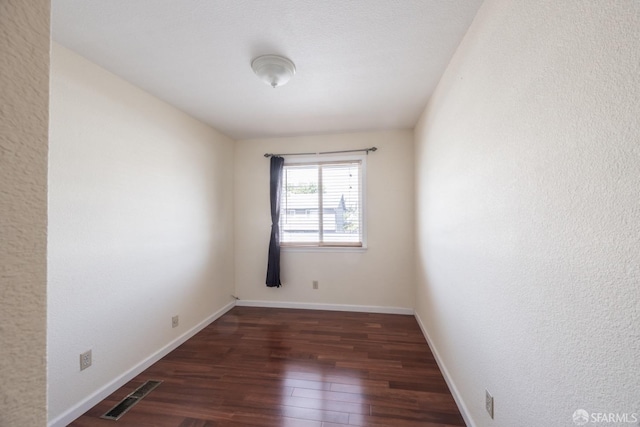 spare room featuring wood finished floors, visible vents, and baseboards