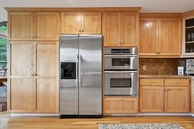 kitchen featuring stone counters, decorative backsplash, stainless steel appliances, and light wood-type flooring