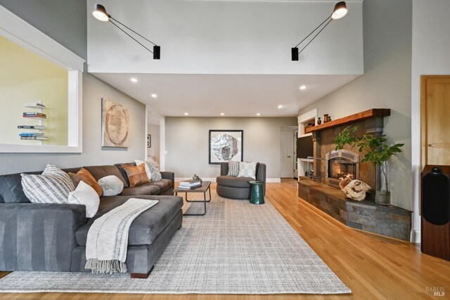 living area featuring baseboards, recessed lighting, wood finished floors, and a warm lit fireplace