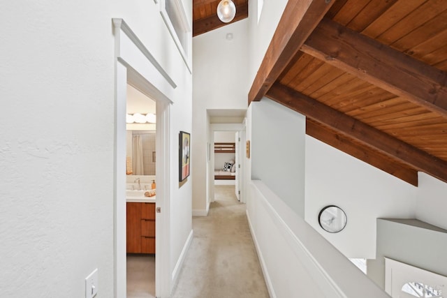 corridor featuring light colored carpet, a sink, vaulted ceiling with beams, and wooden ceiling
