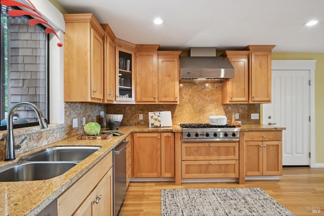 kitchen featuring wall chimney range hood, stainless steel appliances, light wood-style flooring, and a sink