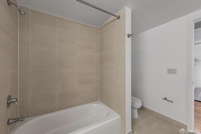 bathroom featuring tile patterned flooring, tiled shower / bath combo, and toilet