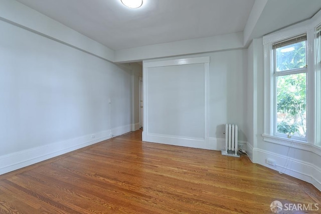 spare room with radiator heating unit, baseboards, and wood finished floors