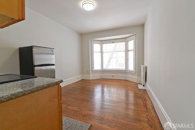 unfurnished dining area featuring radiator, dark wood-style floors, and baseboards