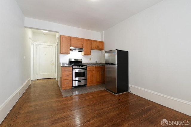 kitchen featuring stainless steel appliances, dark wood-type flooring, a sink, under cabinet range hood, and baseboards