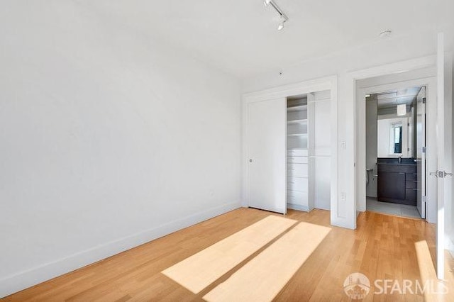 unfurnished bedroom with light wood-type flooring, a closet, and track lighting